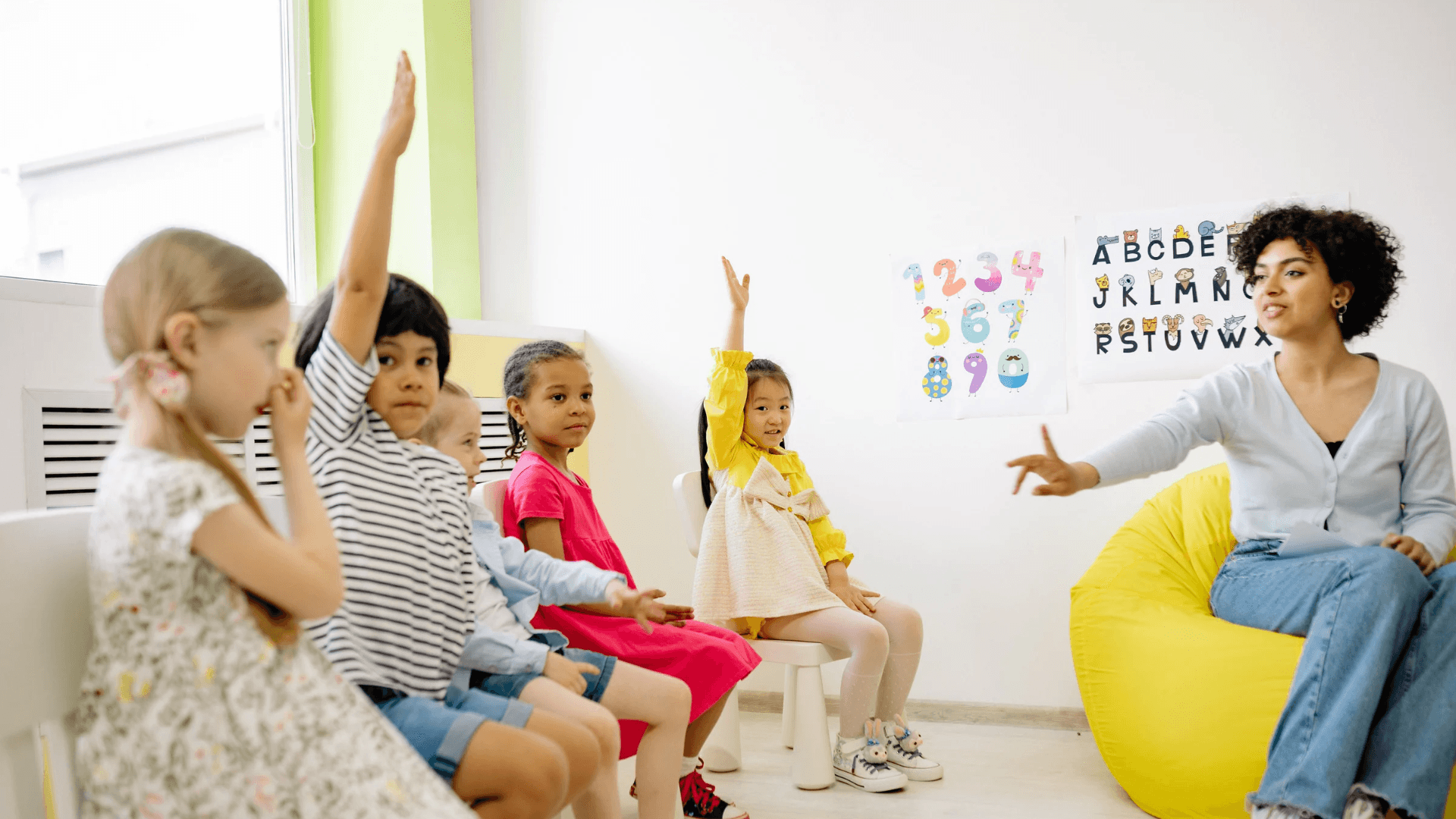 A teacher leading a group of young children in a bright, colourful classroom